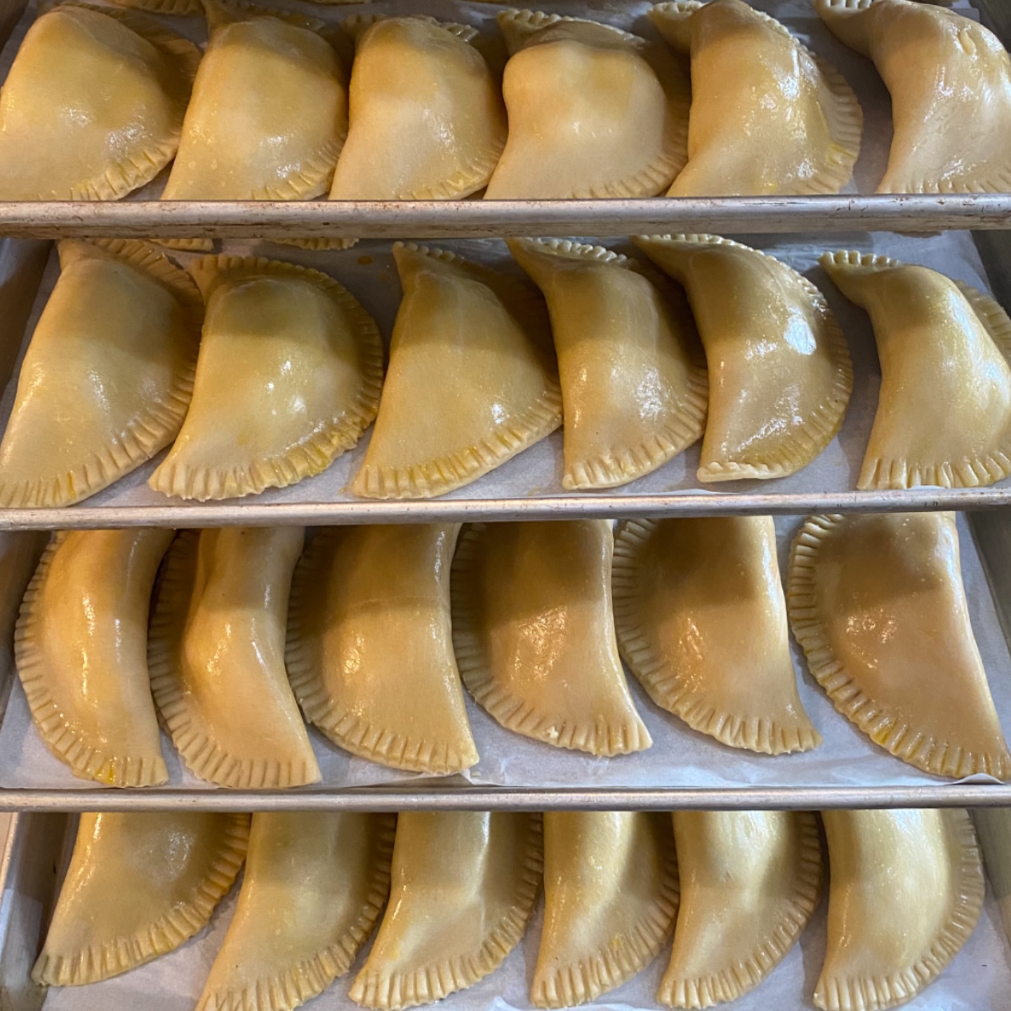 Rows of handmade Peruvian-style empanadas with perfectly crimped golden dough arranged on baking trays
