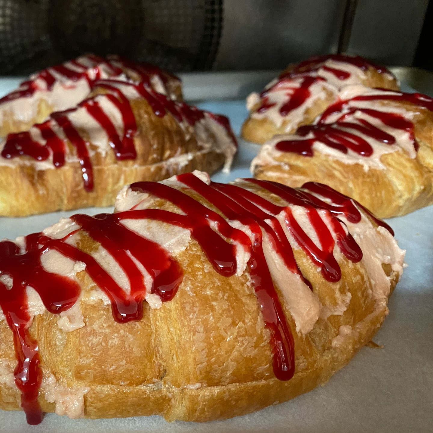 Golden raspberry croissants filled with cream and topped with a vibrant red raspberry drizzle, fresh from the oven