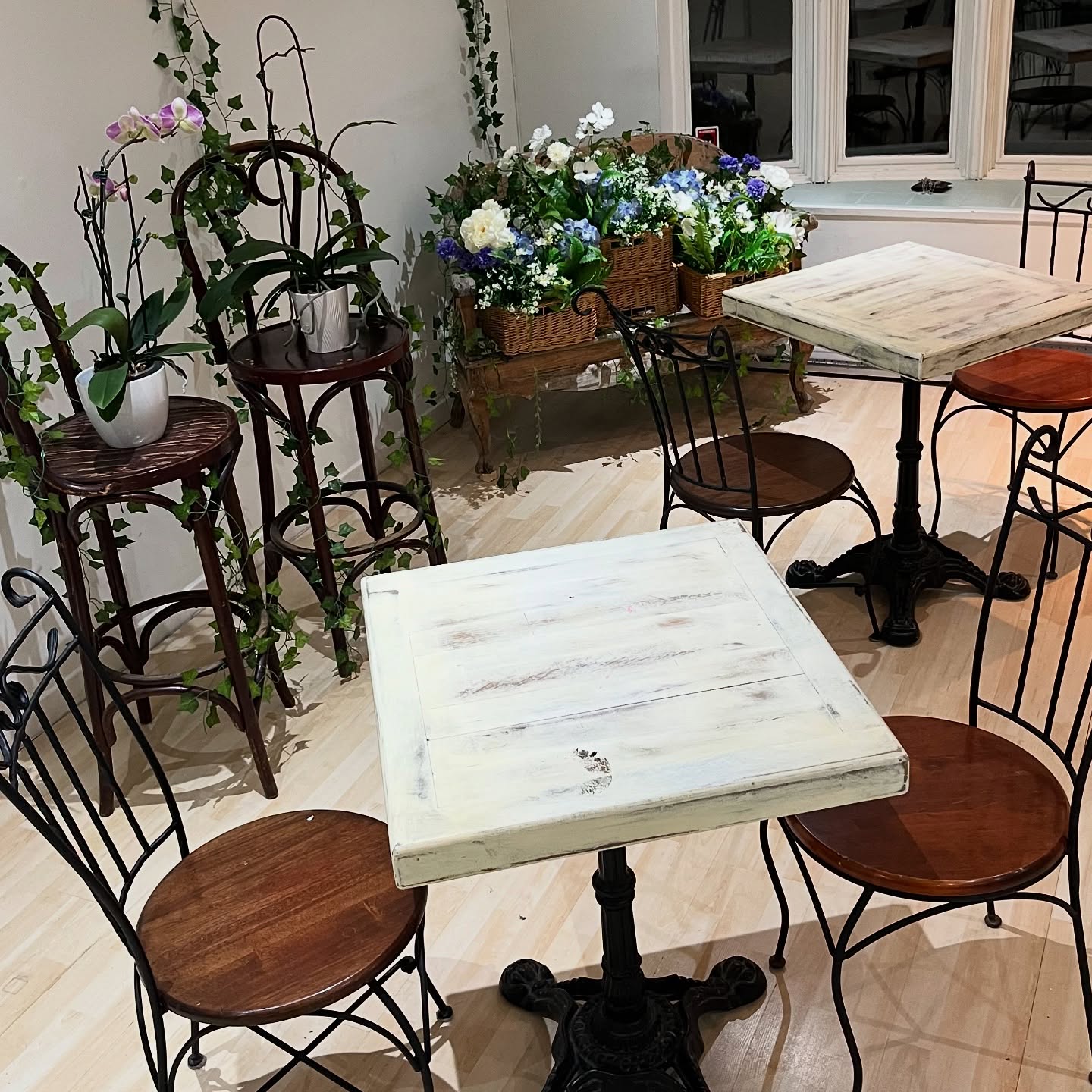 Charming bistro-style seating area inside Sainte Marie Pâtisserie with wrought iron chairs, whitewashed tables, and fresh flower arrangements