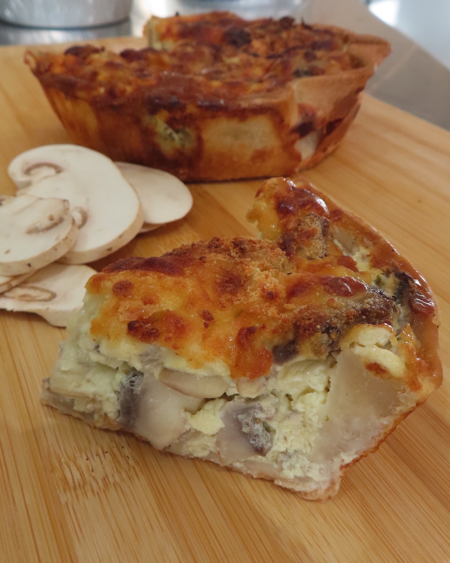 Mushroom quiche sliced with fresh mushrooms on wood board