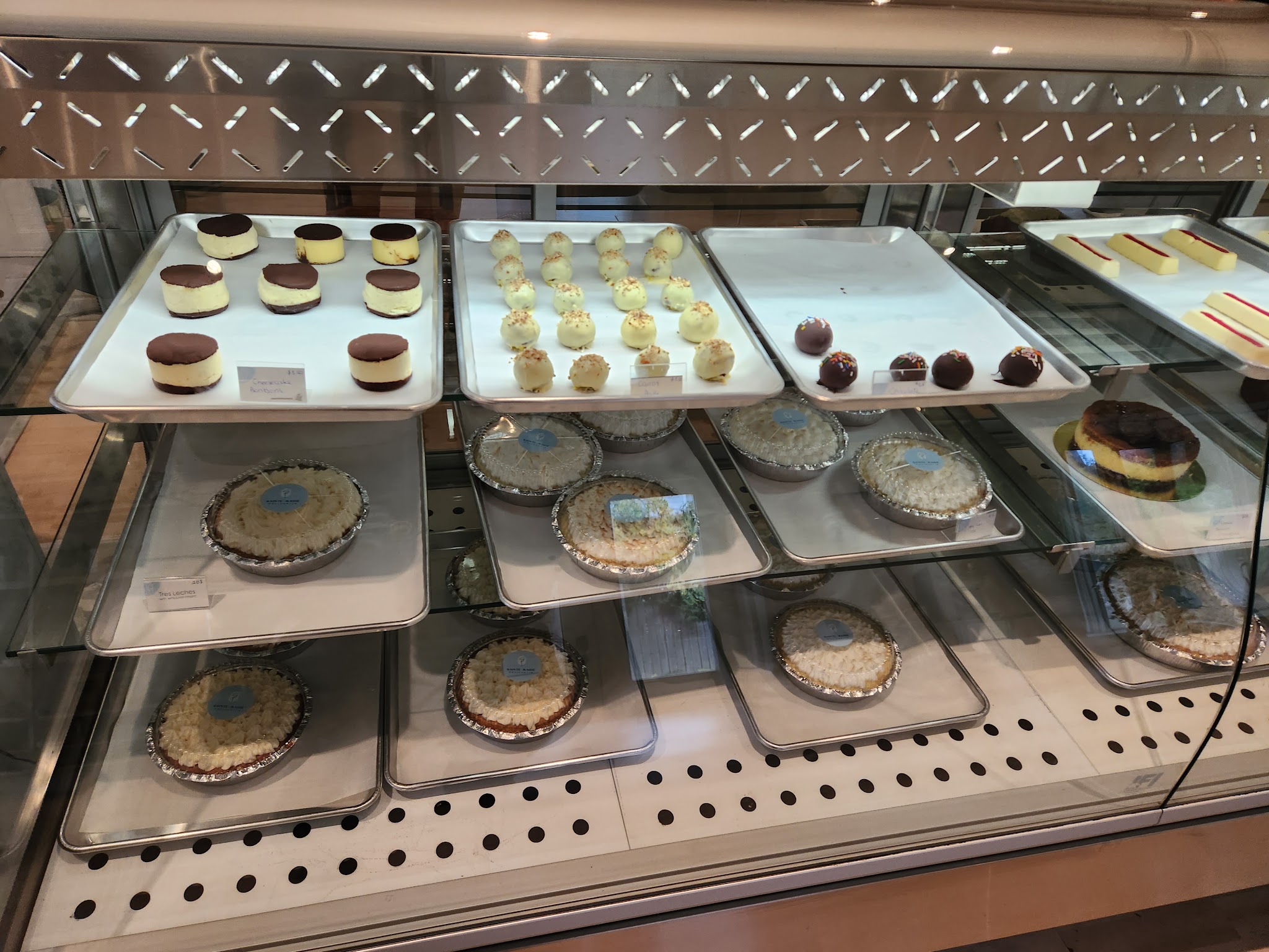 Pastry display case showcasing alfajores with coconut, white chocolate truffles, fruit tarts, and layered cakes